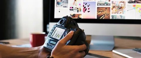 Man holding camera in front of computer screen